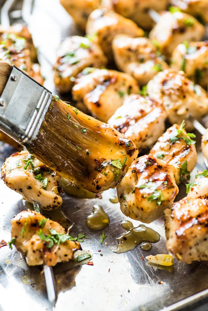 A brush covering chicken kabobs with a honey lime cilantro sauce.
