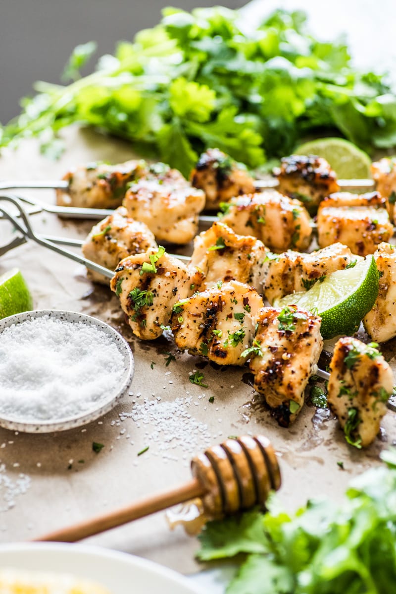 Grilled chicken kabobs on a table garnished with cilantro, salt and pepper.