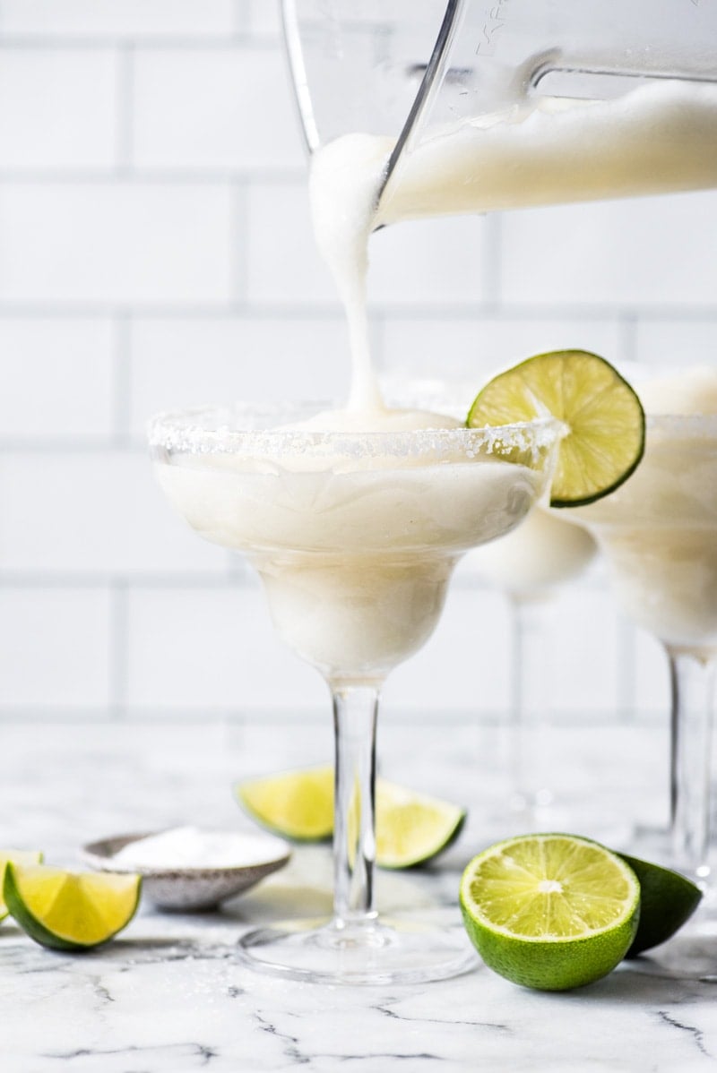 A frozen margarita being poured into a glass from a blender.