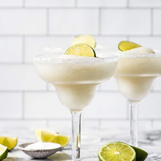Frozen margaritas in glasses topped with lime wedges.