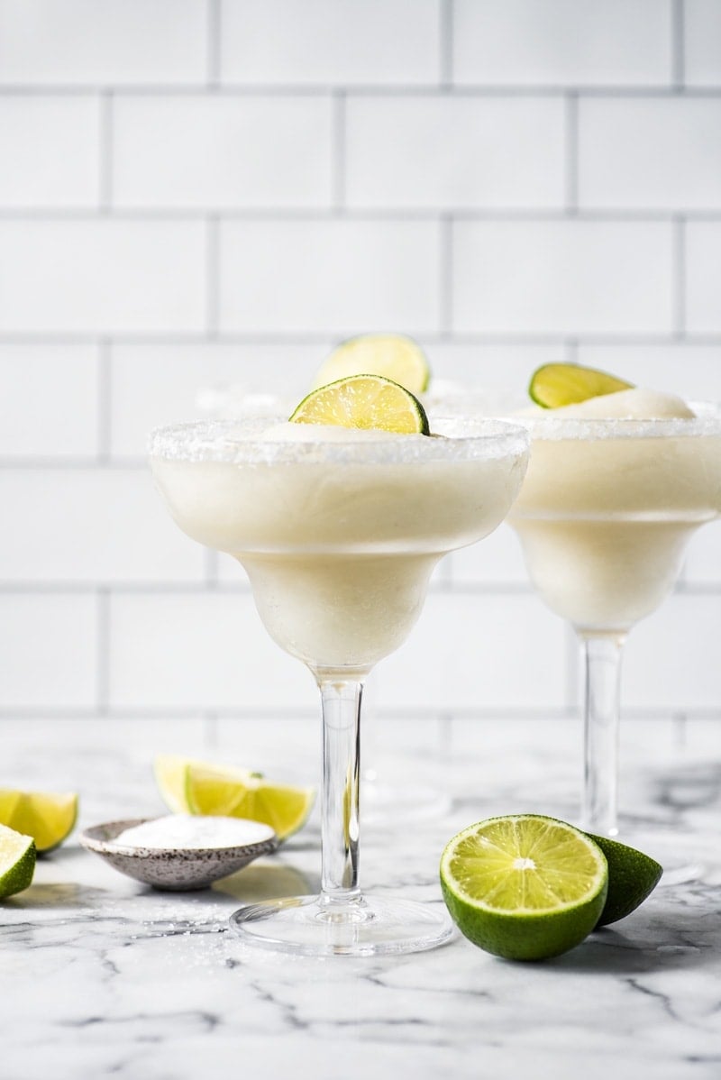 Frozen margaritas in glasses topped with lime wedges.