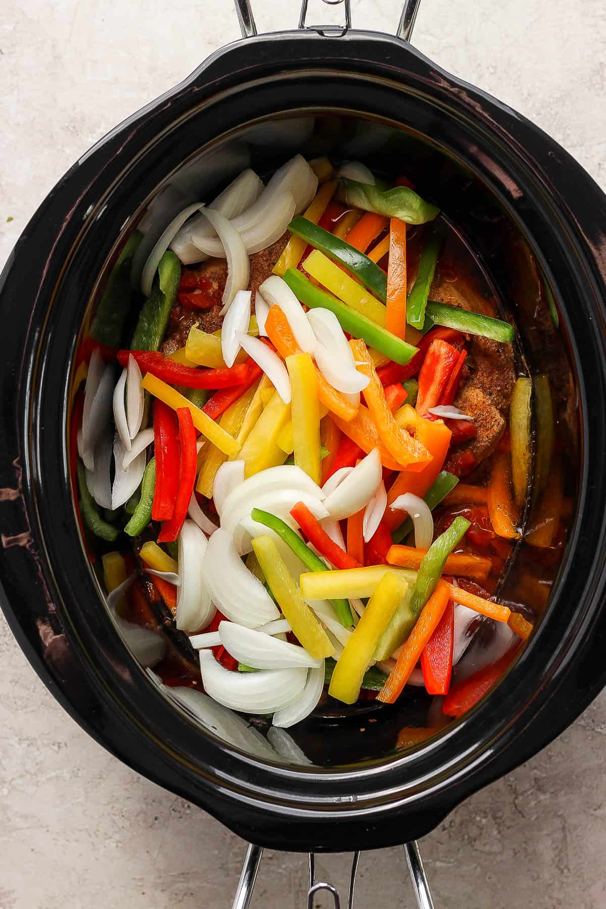 Bell peppers and onions in a slow cooker on top of chicken breasts.