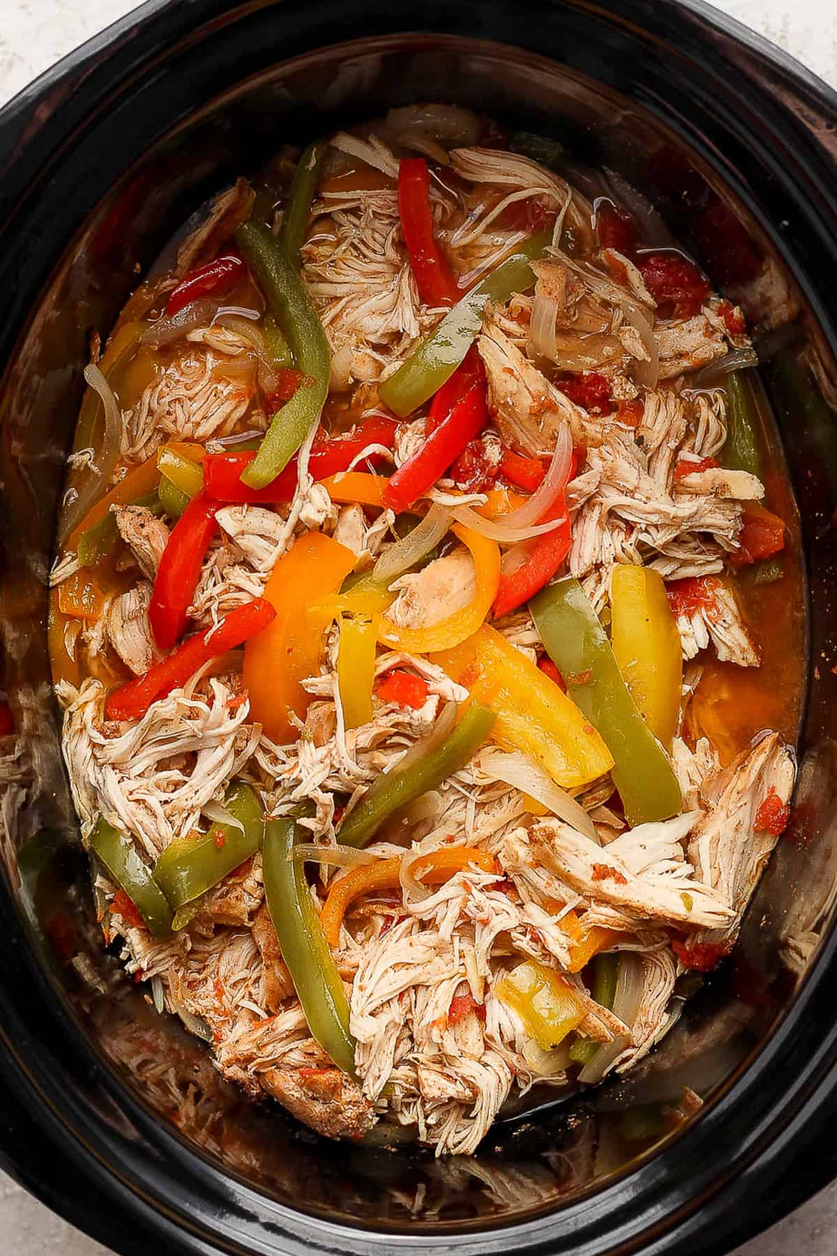 Crockpot chicken fajitas in a slow cooker with bell peppers and onions.