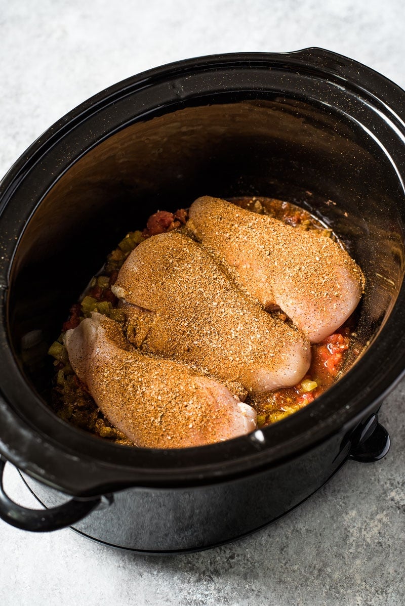 Chicken breasts topped with fajita spice rub in a large black crockpot.