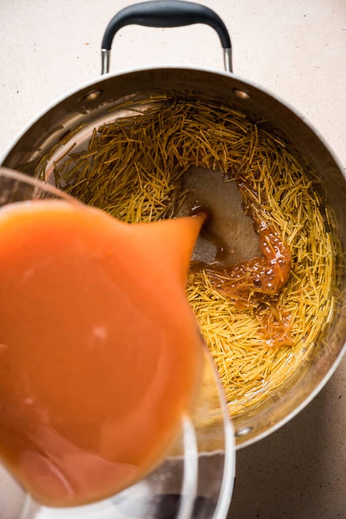 Tomato broth being poured into a pot of toasted noodles for sopa de fideo