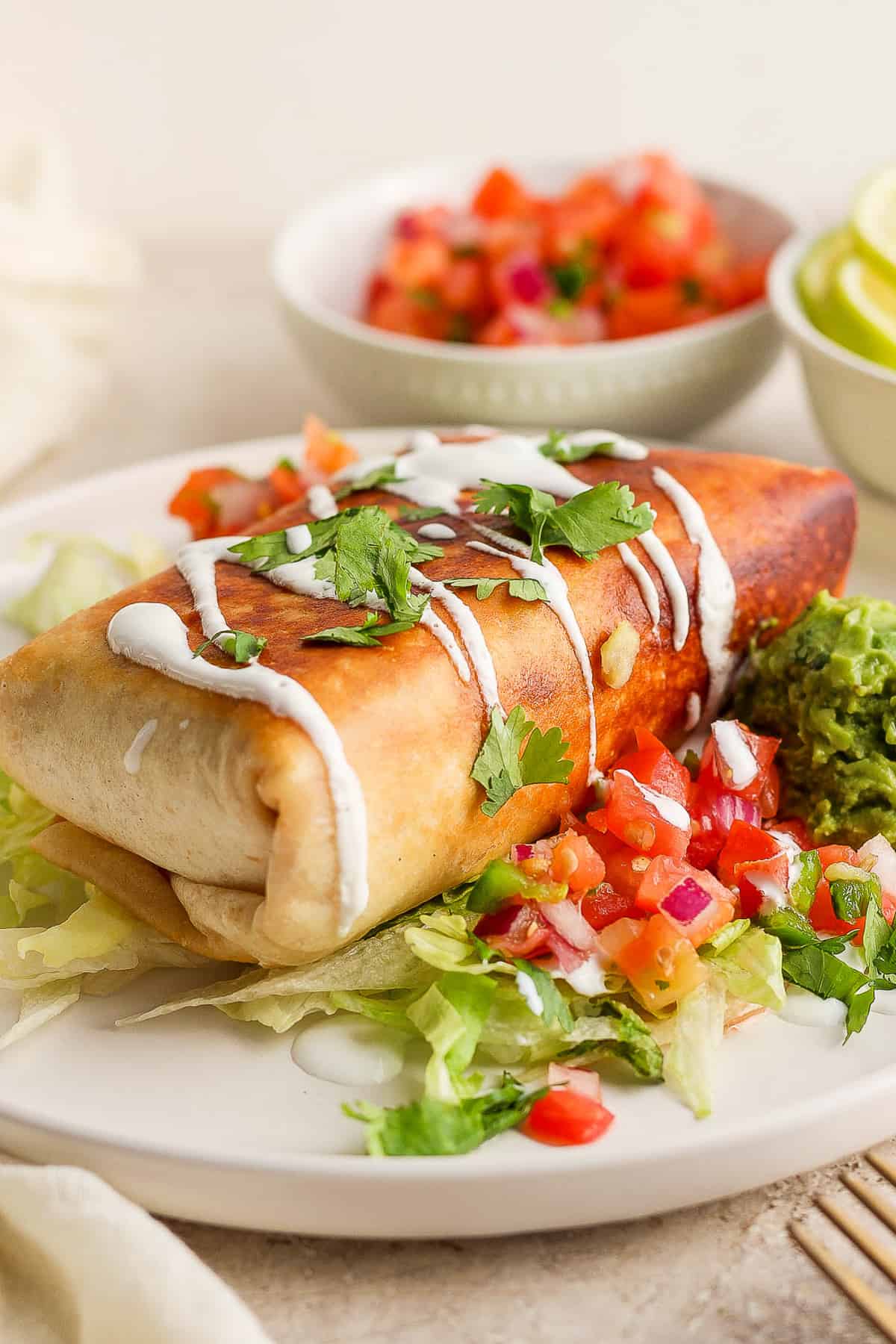 A chicken chimichanga on a bed of shredded lettuce drizzled with mexican crema and served with gucamole and pico de gallo.