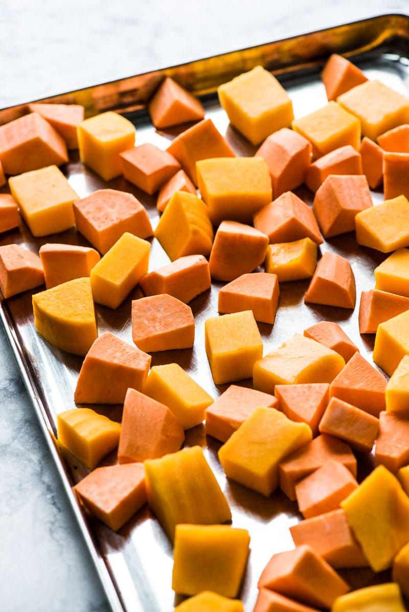 Cut sweet potatoes and butternut squash on a baking sheet to make healthy sweet potato casserole.