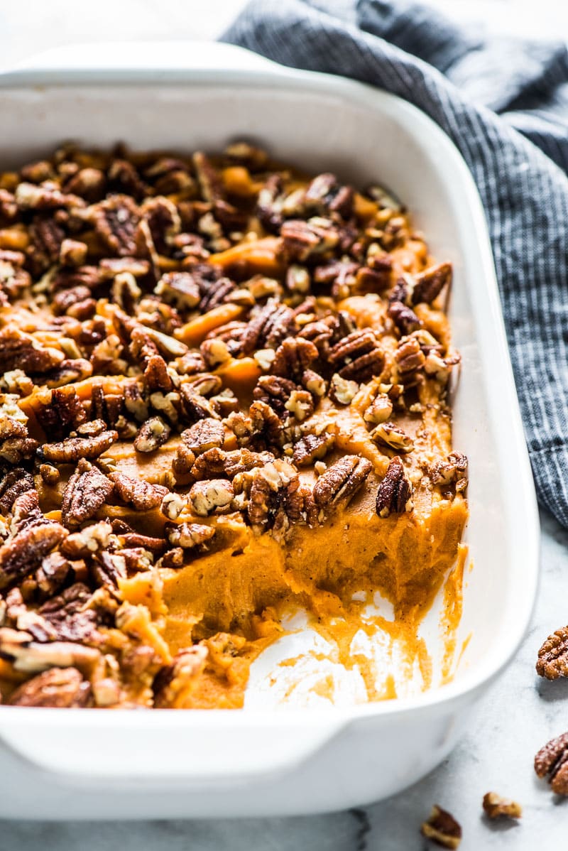 A healthy sweet potato casserole in a white baking dish topped with candied pecans.