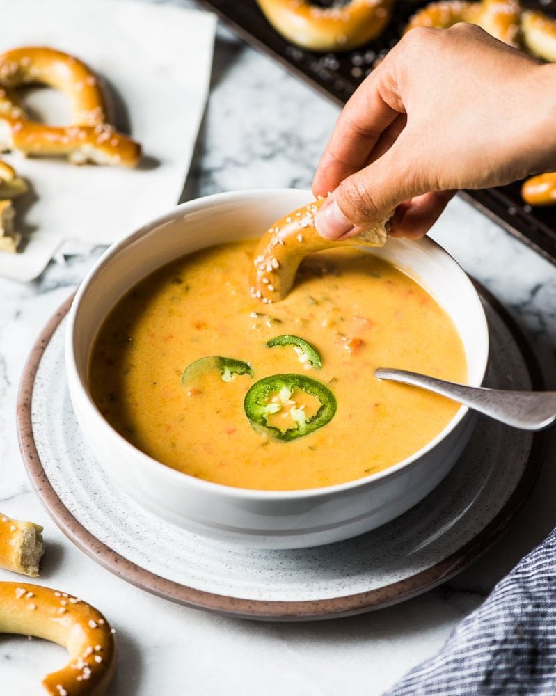 Beer cheese soup in a white bowl topped with thinly sliced jalapenos. 