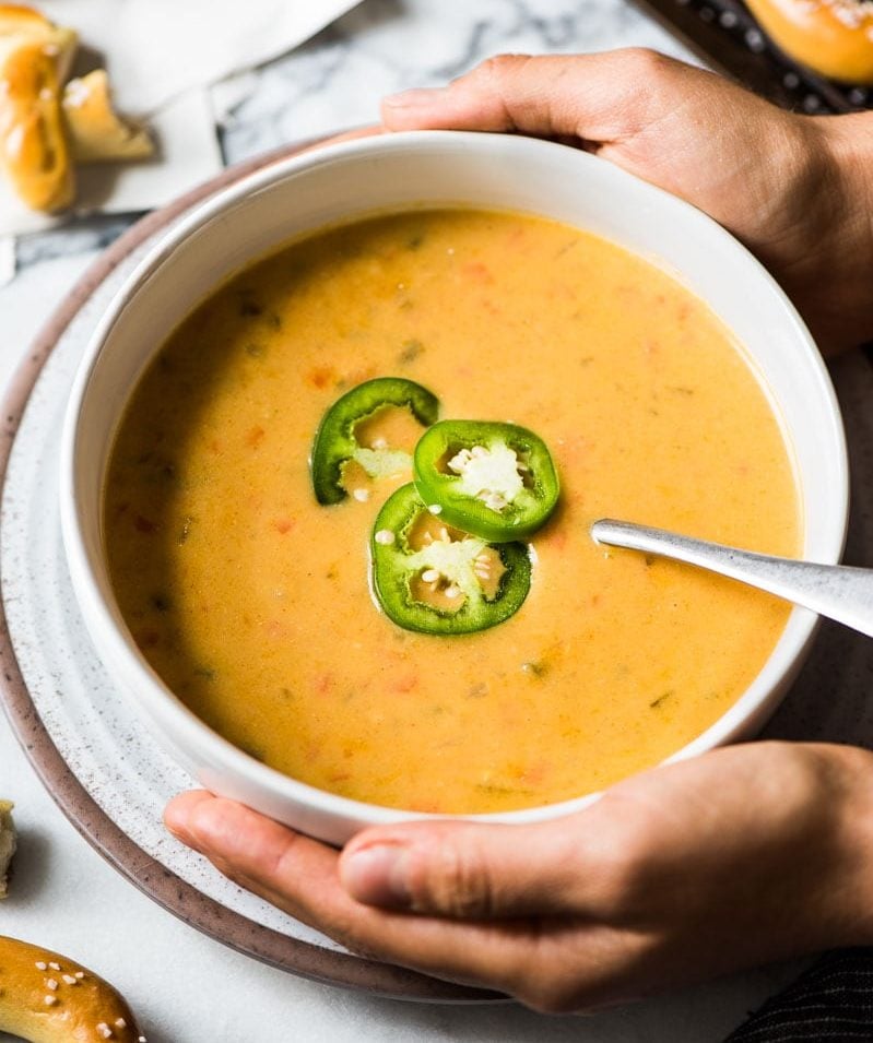 Two hands holding a bowl of warm beer cheese soup.