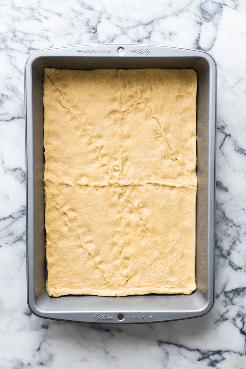 Step one in making sopapilla cheesecake bars. Rectangular 9x13 inch baking dish with crescent roll dough on the bottom.