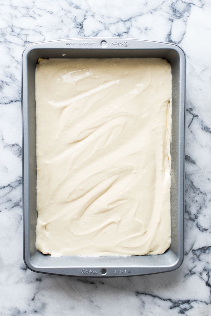 Step two in making sopapilla cheesecake bars. Rectangular 9x13 inch baking dish with cheesecake filling layered on top of crescent roll dough.