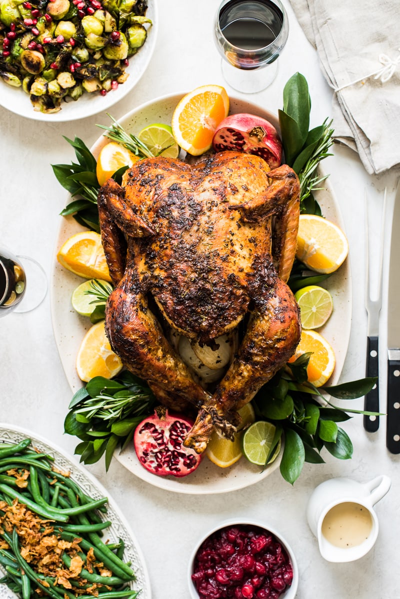 A Thanksgiving turkey on a platter next to green beans and brussel sprouts.