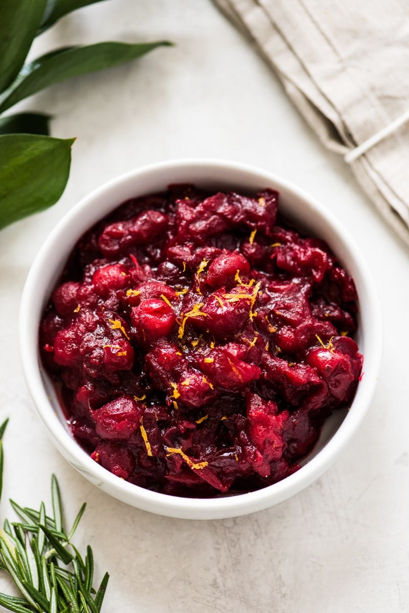 A cranberry sauce recipe in a white bowl topped with orange zest.