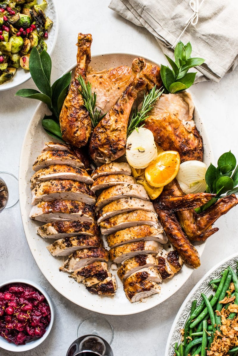 A carved Thanksgiving turkey on a platter next to holiday side dishes.