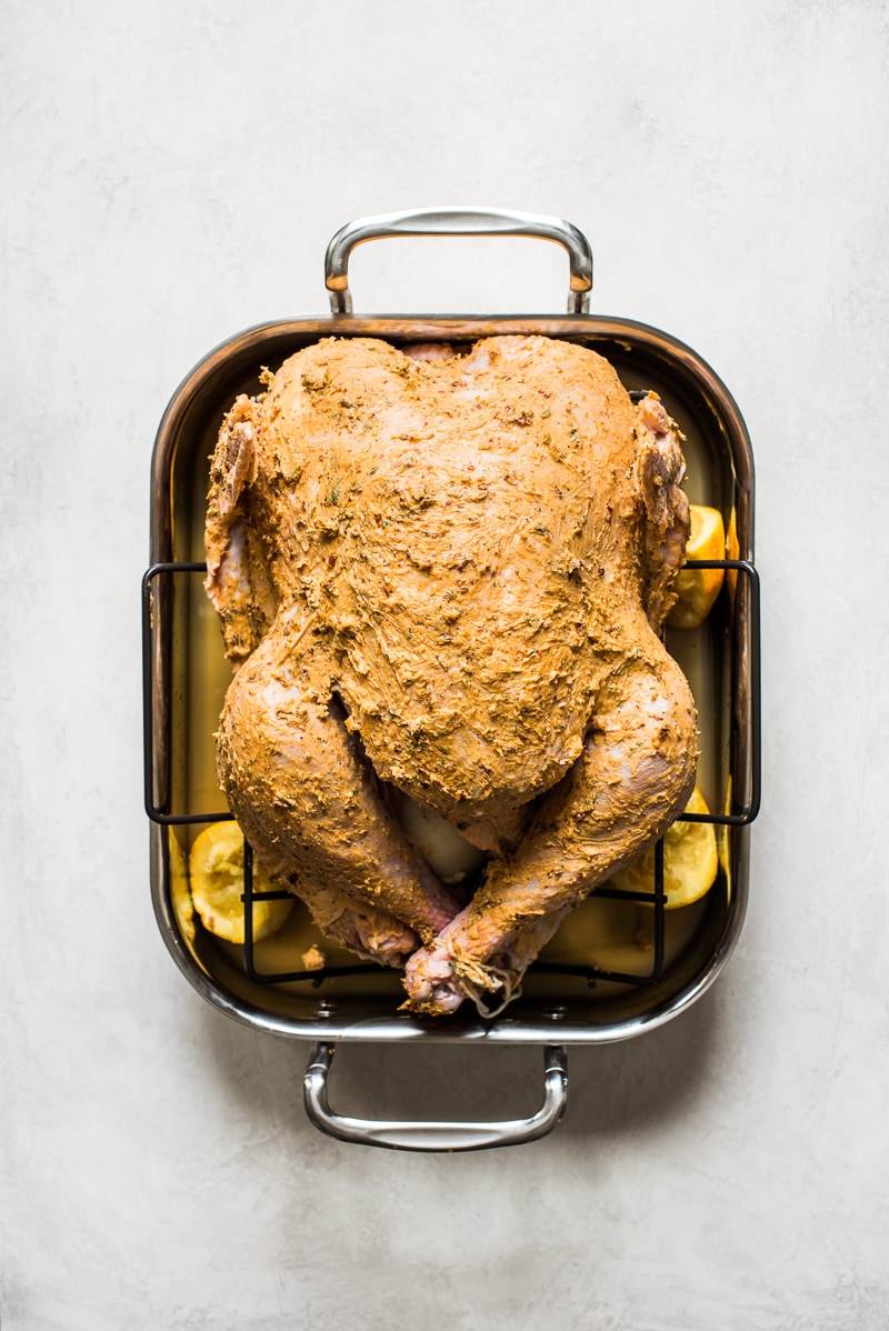 An uncooked Thanksgiving turkey in a roasting pan covered in compound butter.