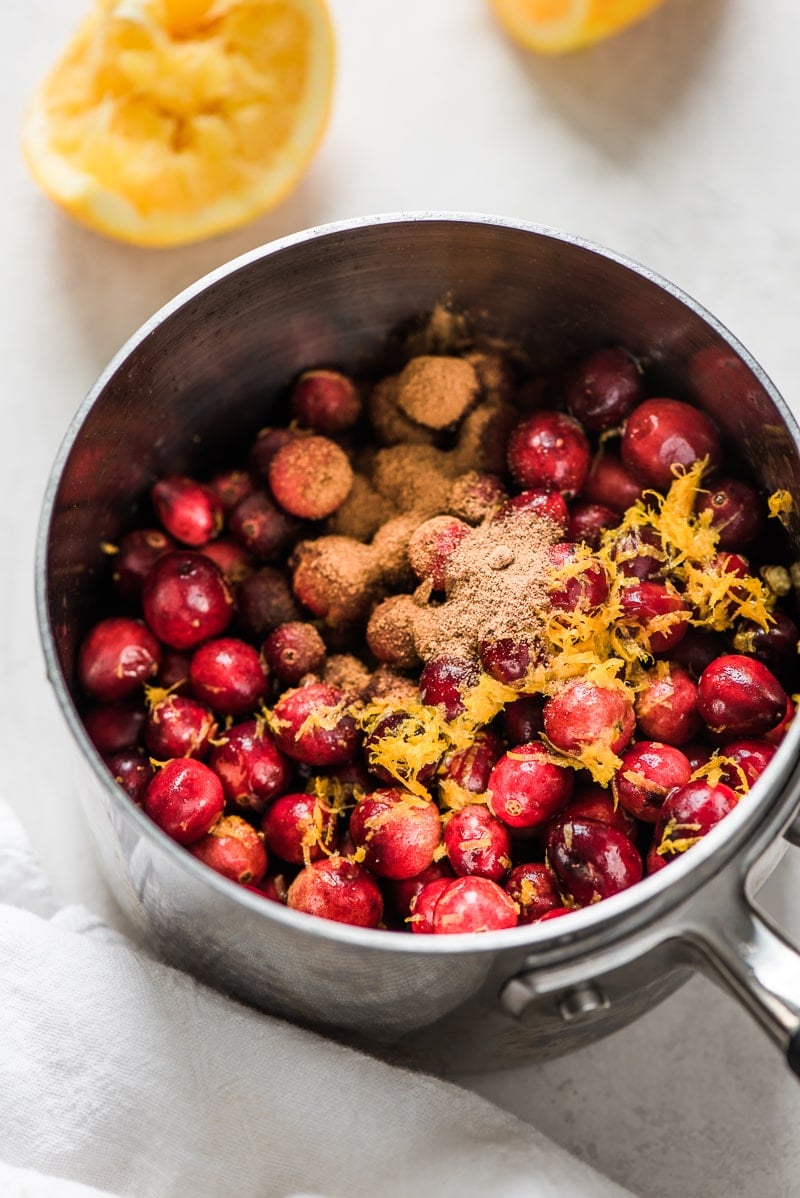 Cranberries in a pot topped with orange zest, orange juice, honey and nutmeg.