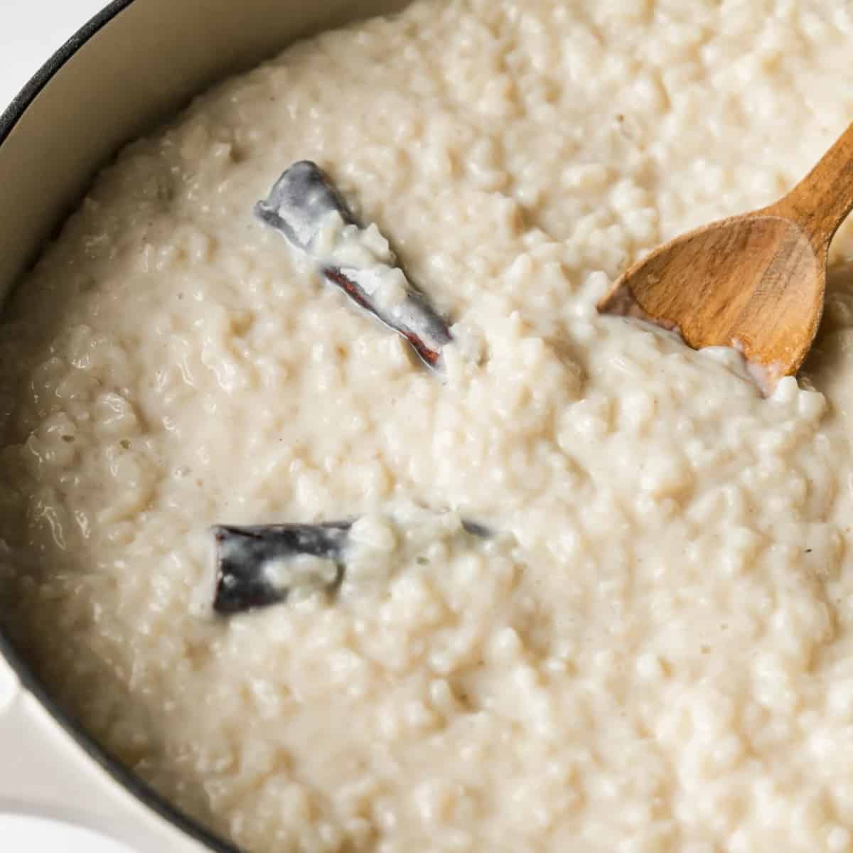 Arroz con leche in a pot being stirred with a wooden spoon.