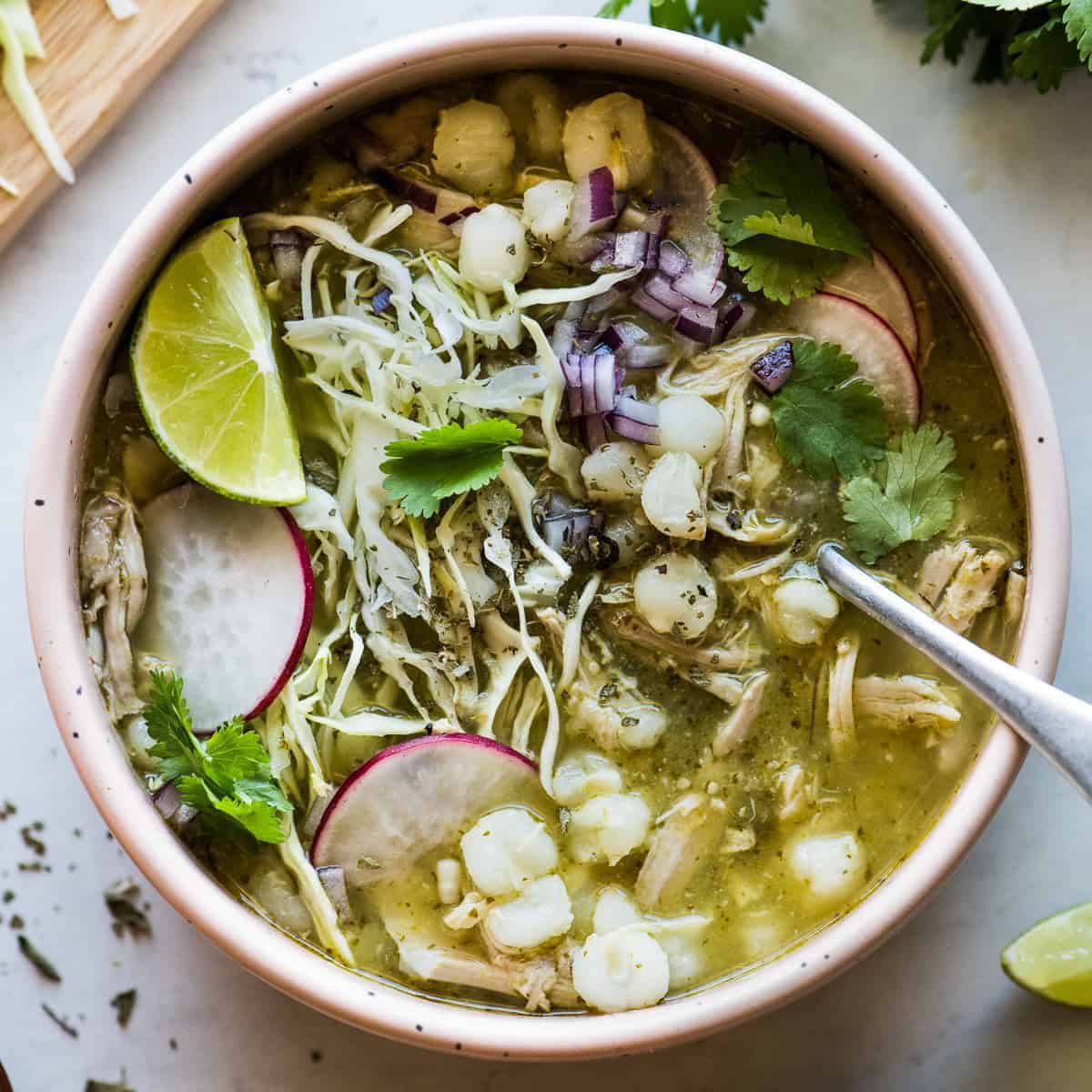 Chicken pozole verde in a bowl with various toppings like shredded cabbage, cilantro, sliced radishes, and diced red onions.
