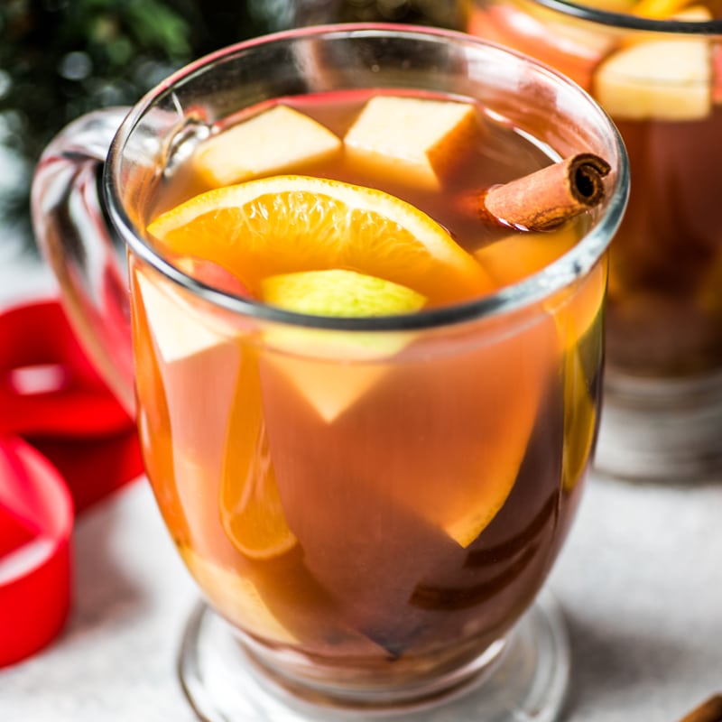 A mug of ponche filled with fruit and a cinnamon stick.