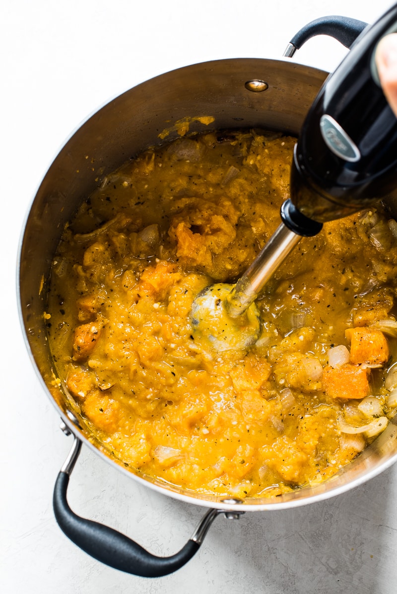 Roasted butternut squash, onions and vegetable stock being blended using an immersion blender in a large stockpot