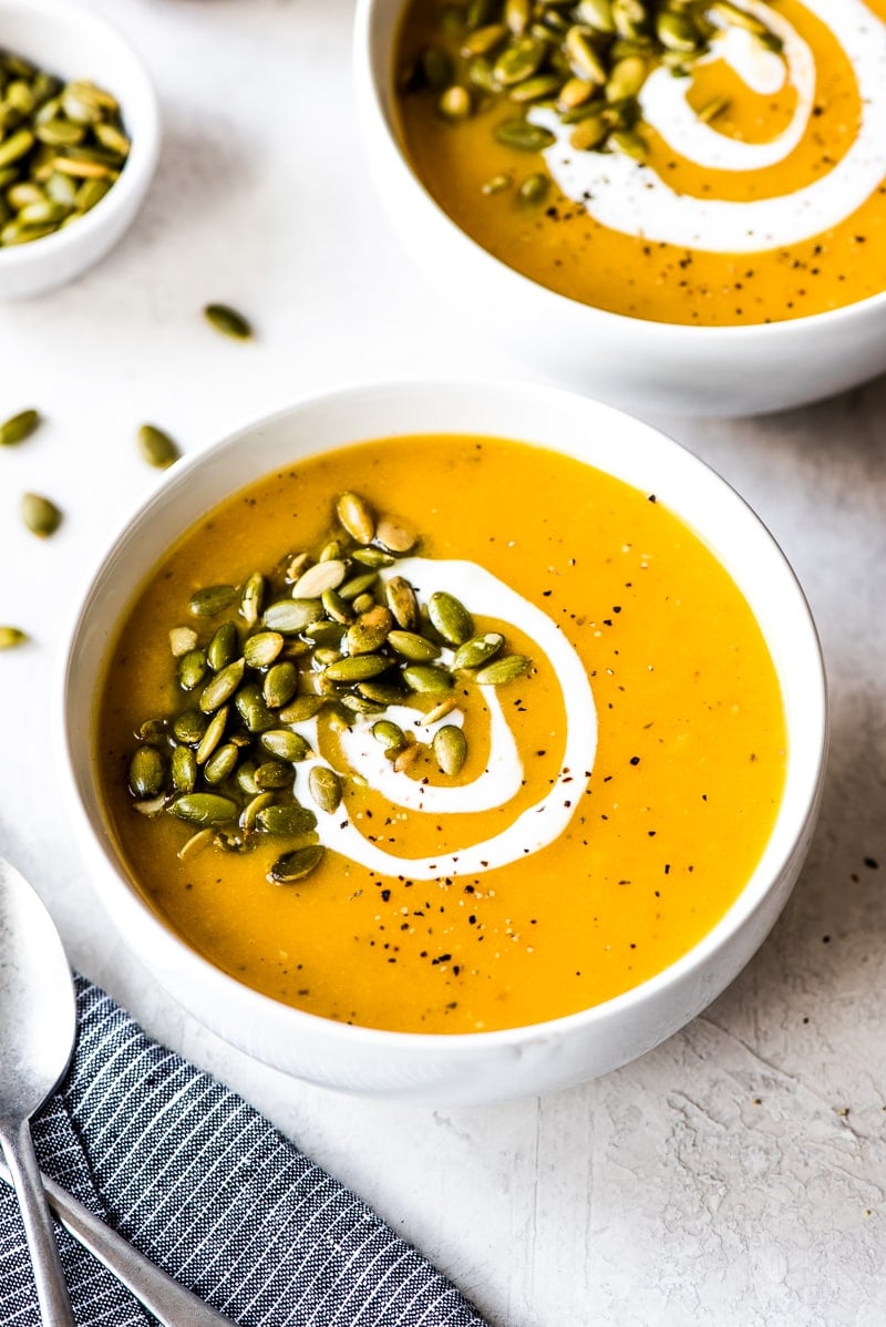 Two bowls of Roasted Butternut Squash Soup on a white table.