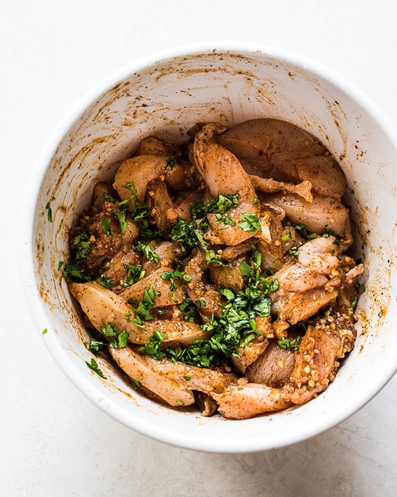 Sliced chicken breast in a white bowl in marinade made with cilantro.