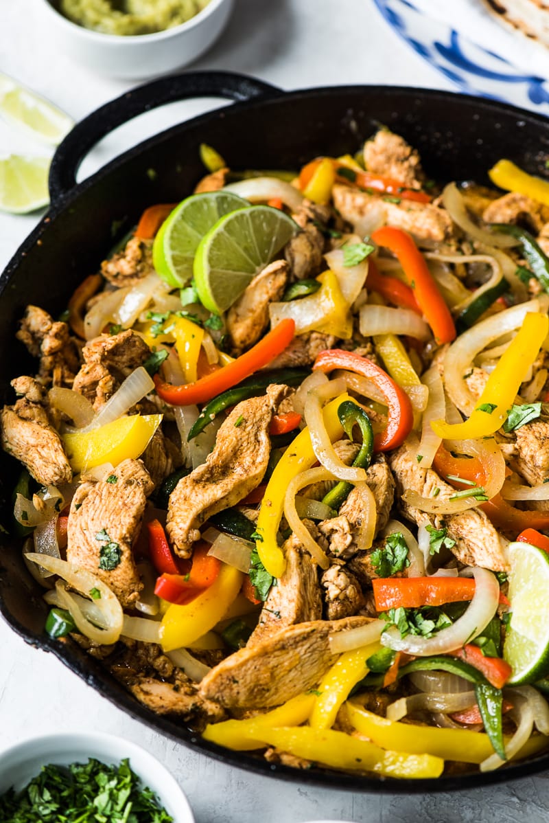 Cooked chicken fajitas with sliced bell peppers and onions in a cast iron skillet.