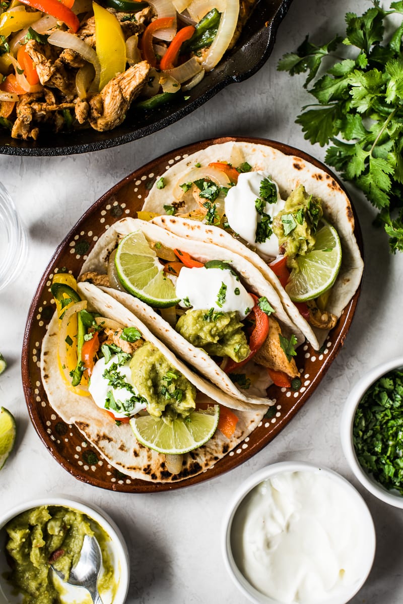 Chicken fajita tacos topped with sour cream, guacamole and chopped cilantro.