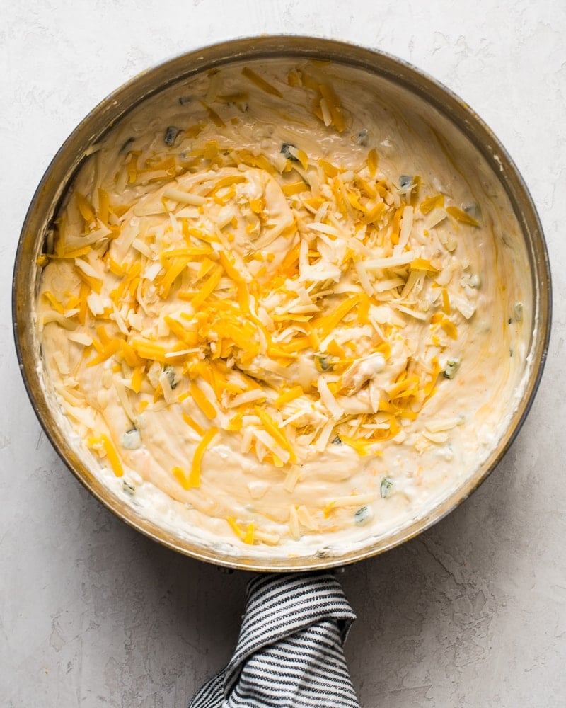 A saute pan with shredded cheese and cream cheese.