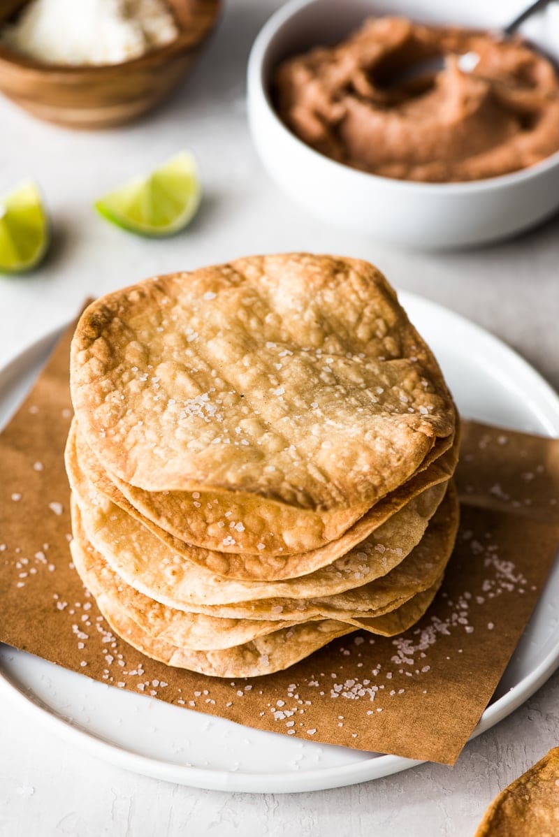 Tostada shells on a white plate next to refried beans and limes.