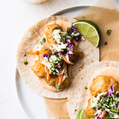 Baja fish tacos on a plate topped with chipotle mayo and a creamy slaw.