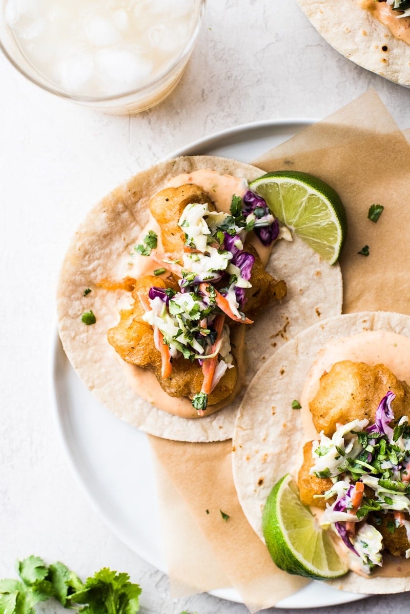 Baja fish tacos on a plate topped with chipotle mayo and a creamy slaw.