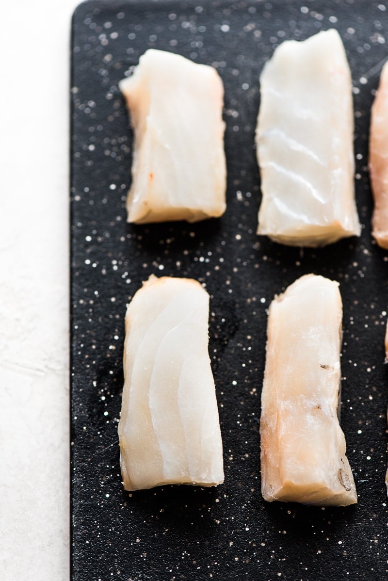 Sliced strips of Atlantic Cod on a black cutting board for Baja Fish Tacos recipe.