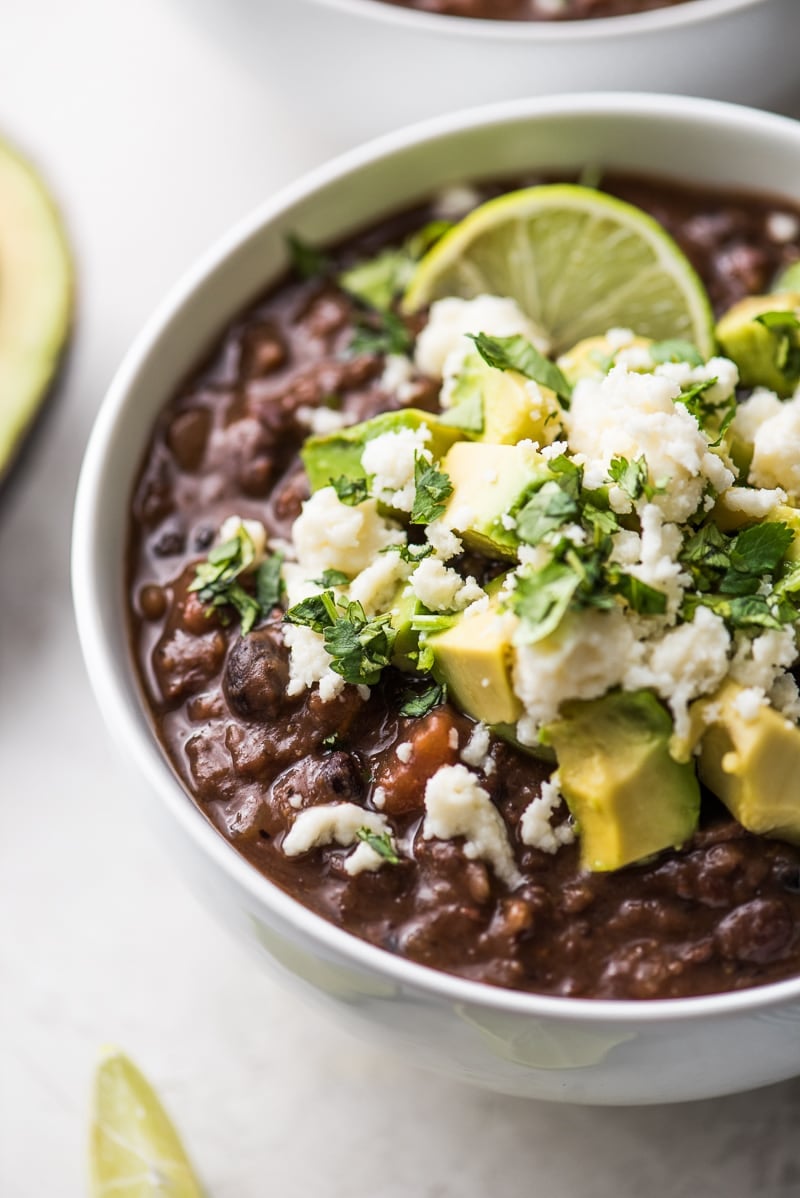 Vegetarian Black Bean Soup in a bowl topped with avocados, cheese, cilantro and a lime wedge.