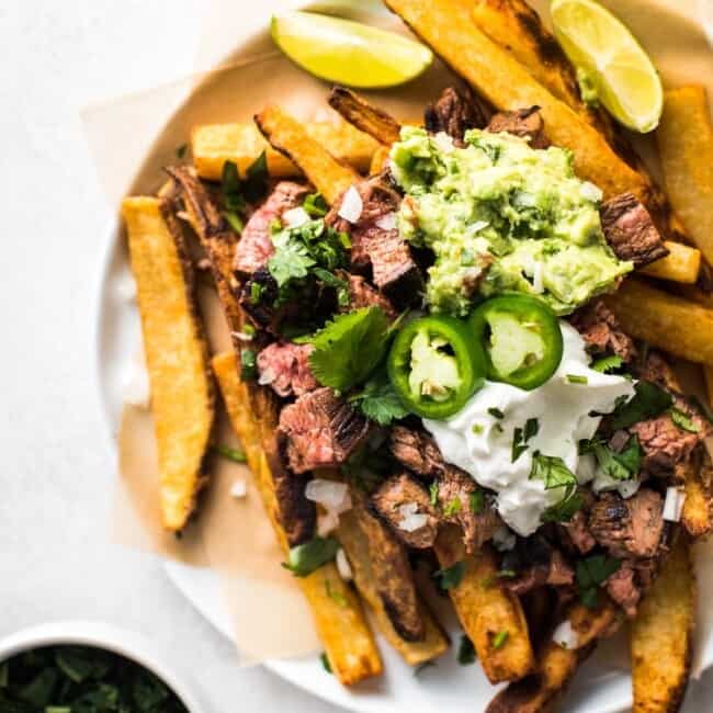 This Carne Asada Fries recipe is a San Diego classic featuring crispy baked fries topped with shredded cheese, tender carne asada, guacamole and sour cream!