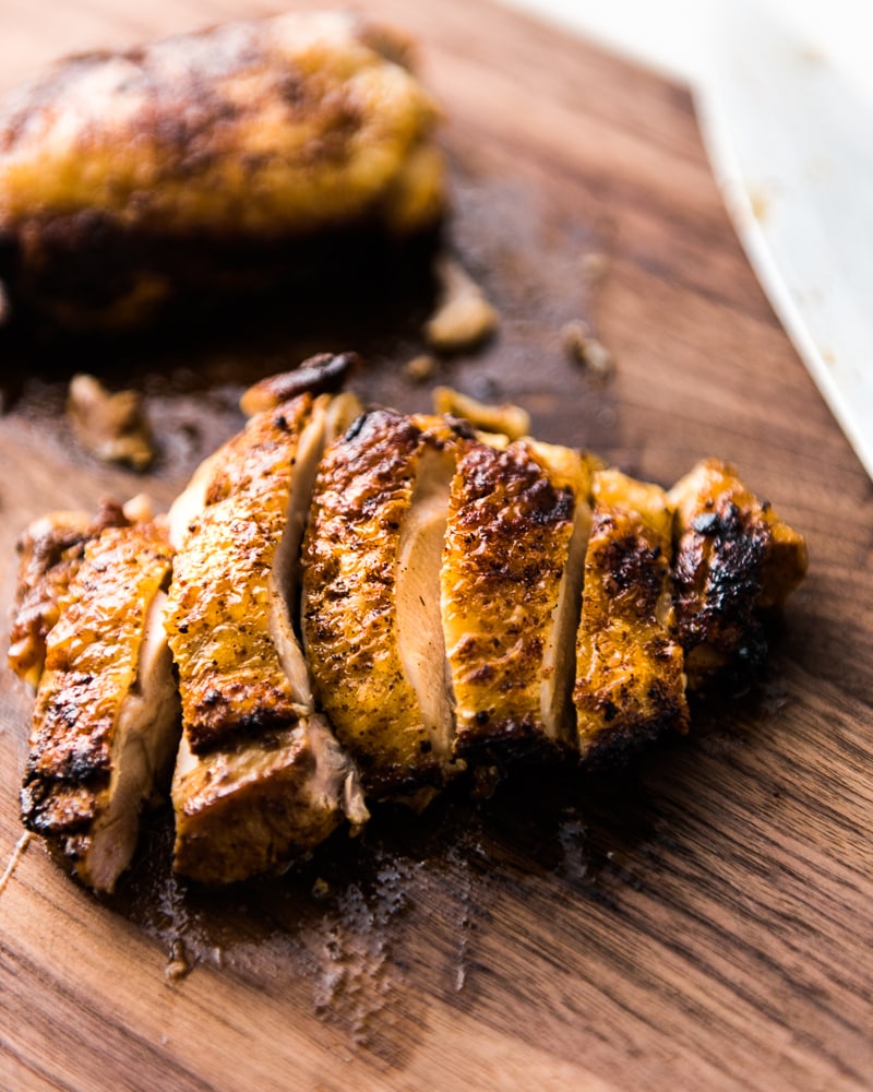 Juicy marinated chicken slices on a brown cutting board for a chicken burrito bowl recipe.