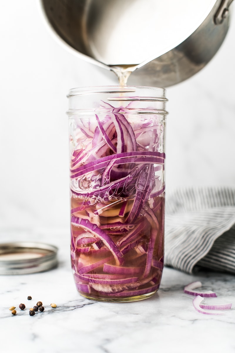 How to pickle onions - sliced red onions in a ball wide-mouth jar with pickling liquid pouring in