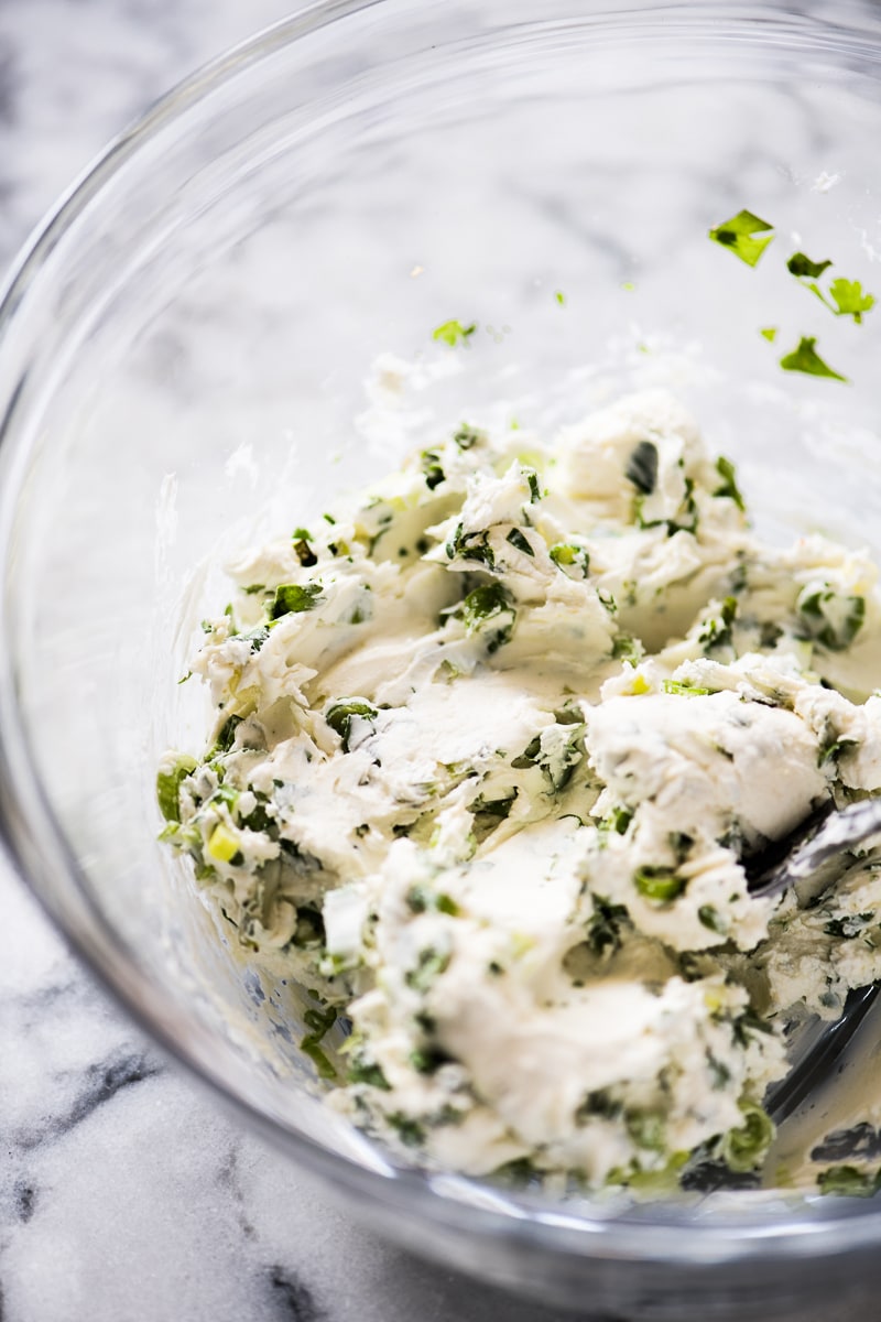 Cream cheese in a bowl mixed together with herbs and spices to be stuffed in jalapeno poppers.