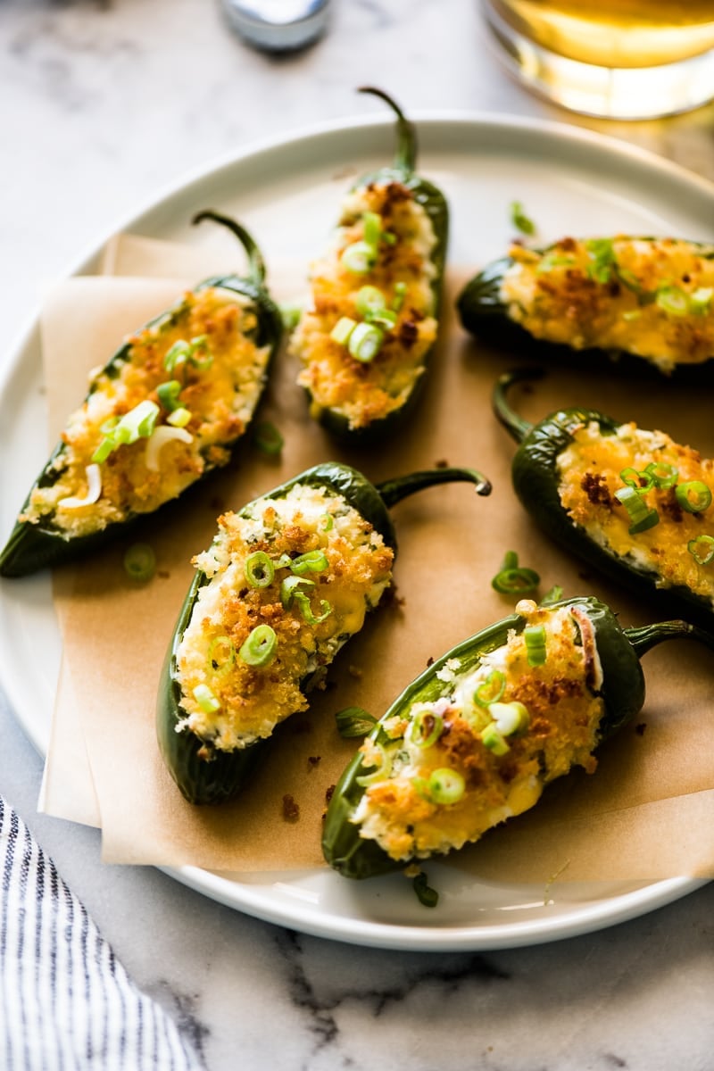Baked Jalapeno Poppers stuffed with cream cheese and topped with panko breadcrumbs and green onions on a white plate.