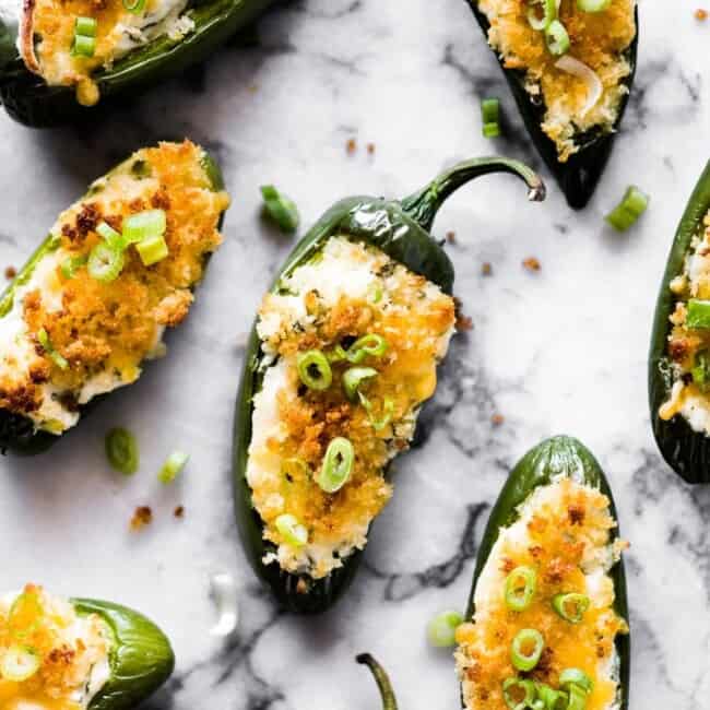 Overhead photo of baked jalapeno poppers topped with breadcrumbs and green onions on a marble countertop.