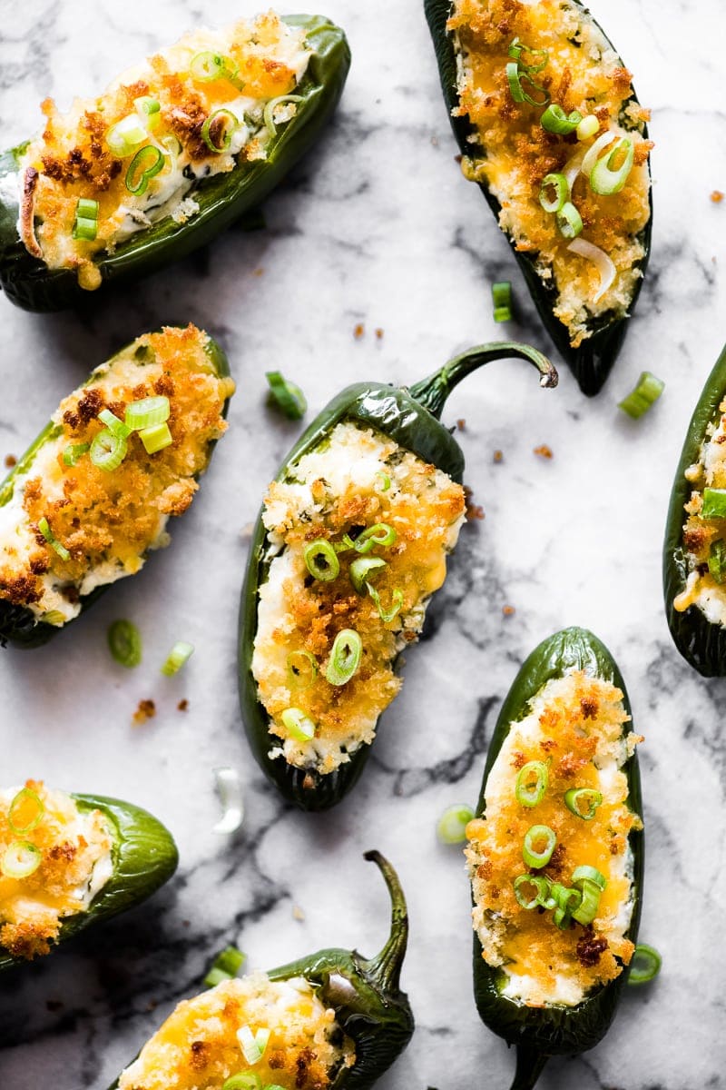Overhead photo of baked jalapeno poppers topped with breadcrumbs and green onions on a marble countertop.