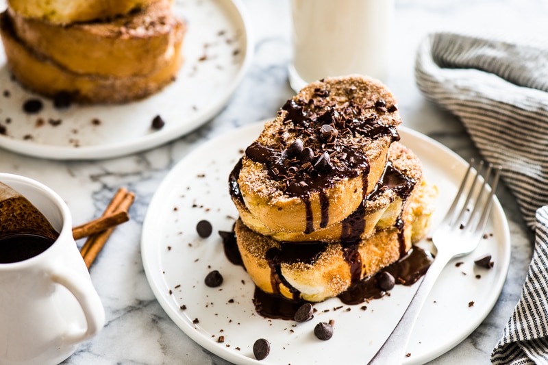 Cinnamon french toast on a white plate topped with Mexican chocolate sauce and a glass of milk in the background.