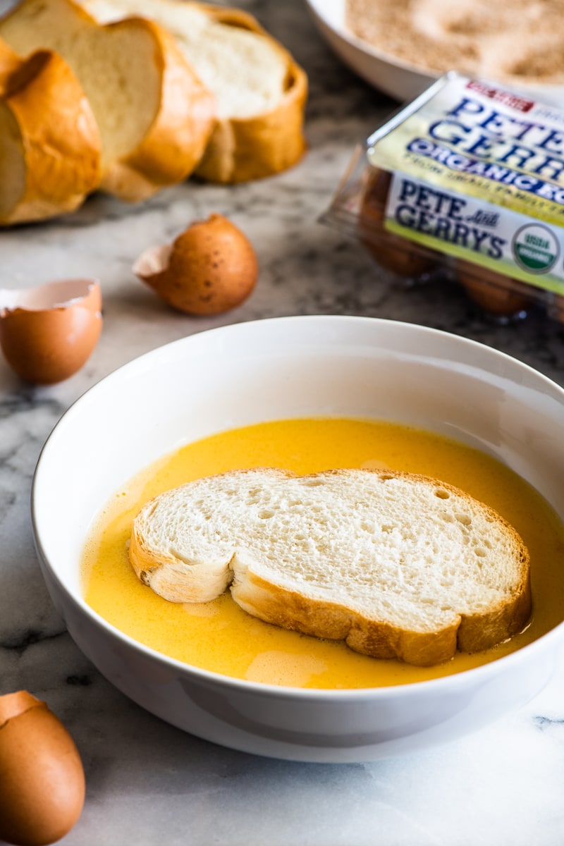 A thick cut slice of french bread soaking in a white bowl of scrambled Pete and Gerry's Organic Eggs.