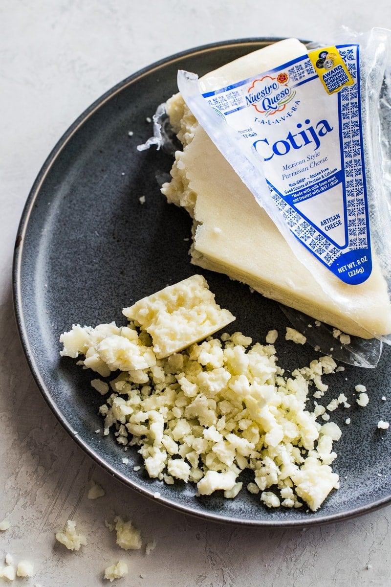 Queso cotija desmenuzado en un plato de piedra gris.