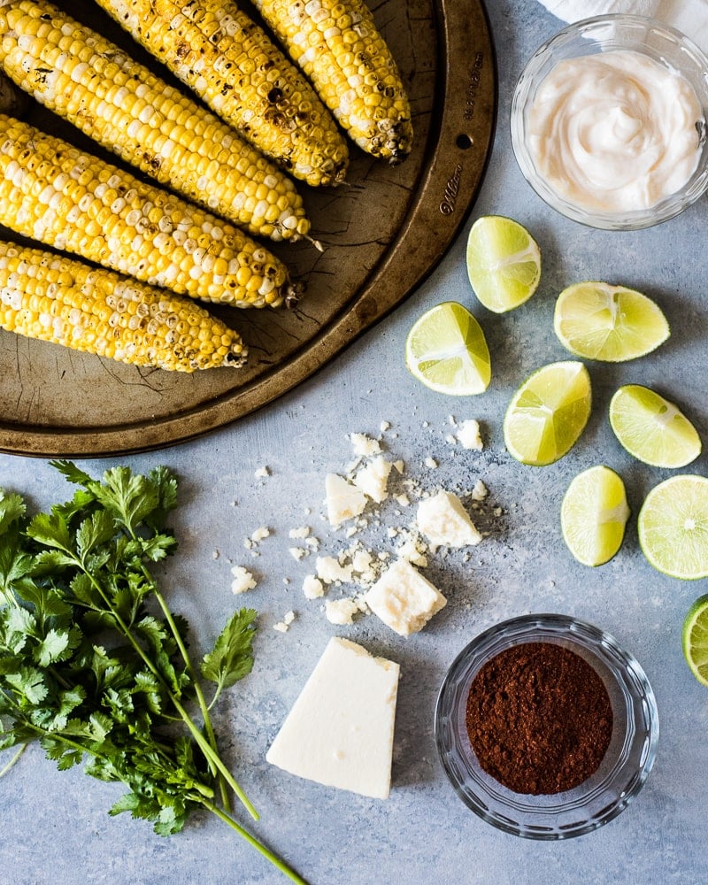 Fromage cotija émietté sur une table avec d'autres ingrédients utilisés pour faire du maïs de rue mexicain.