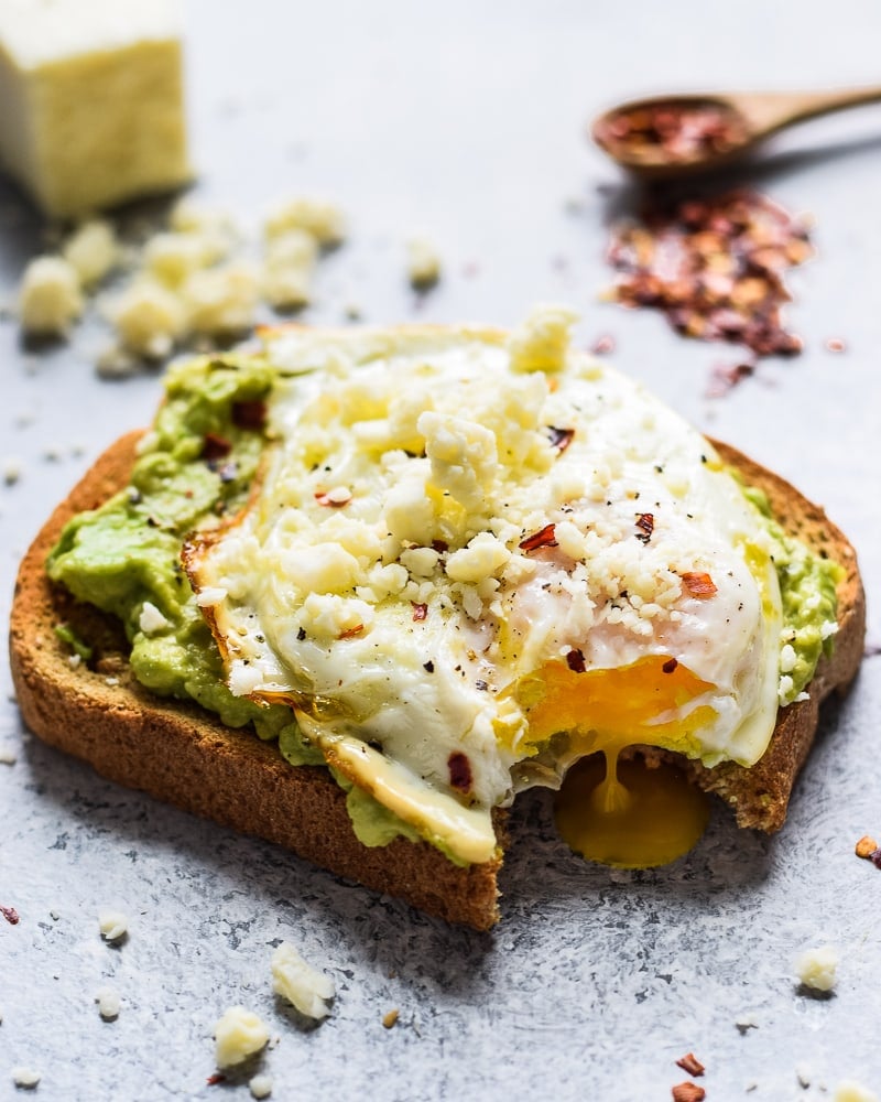 Fromage cotija émietté sur une tranche de pain grillé à l'avocat avec un œuf au plat.