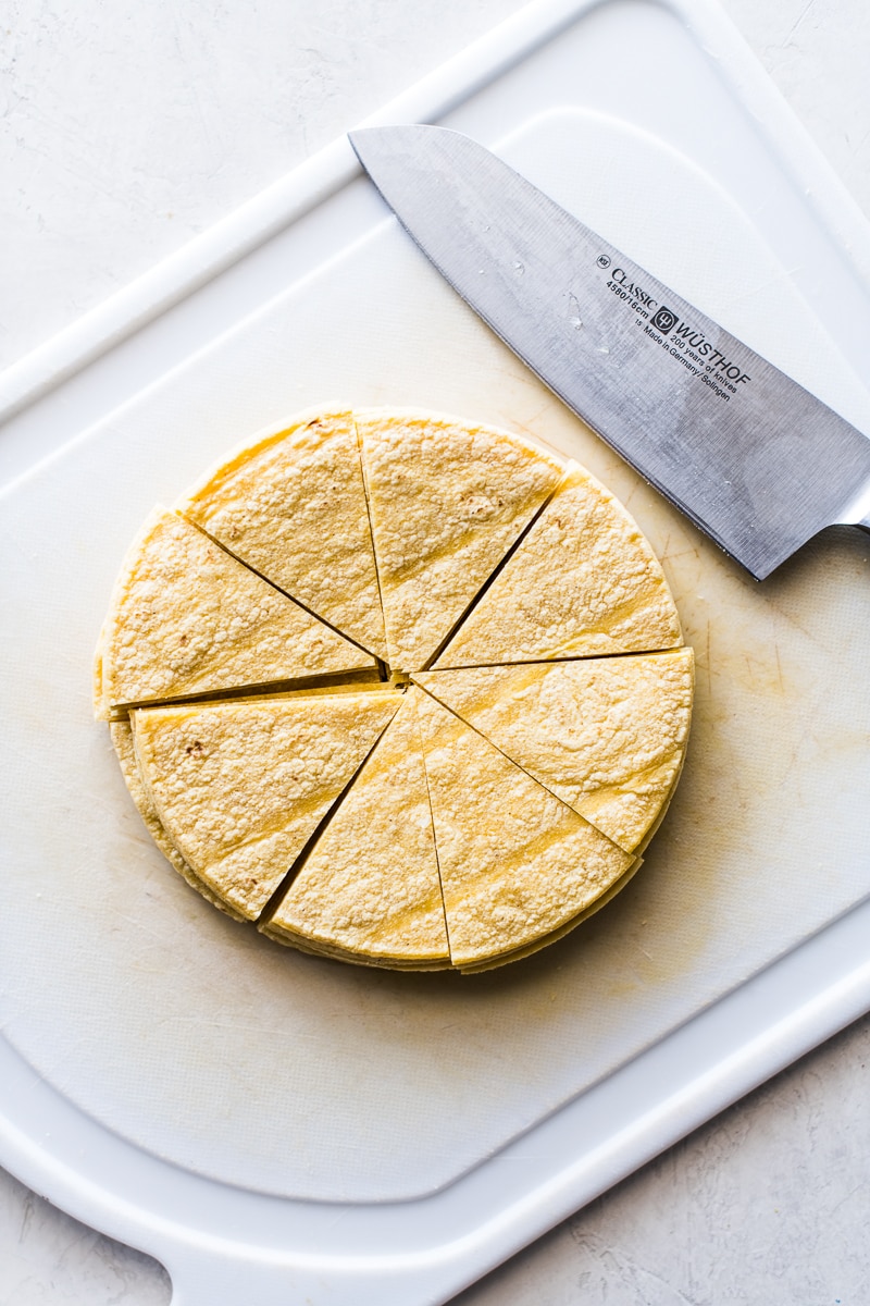 Cut corn tortillas on a white cutting board getting ready to be made into migas.