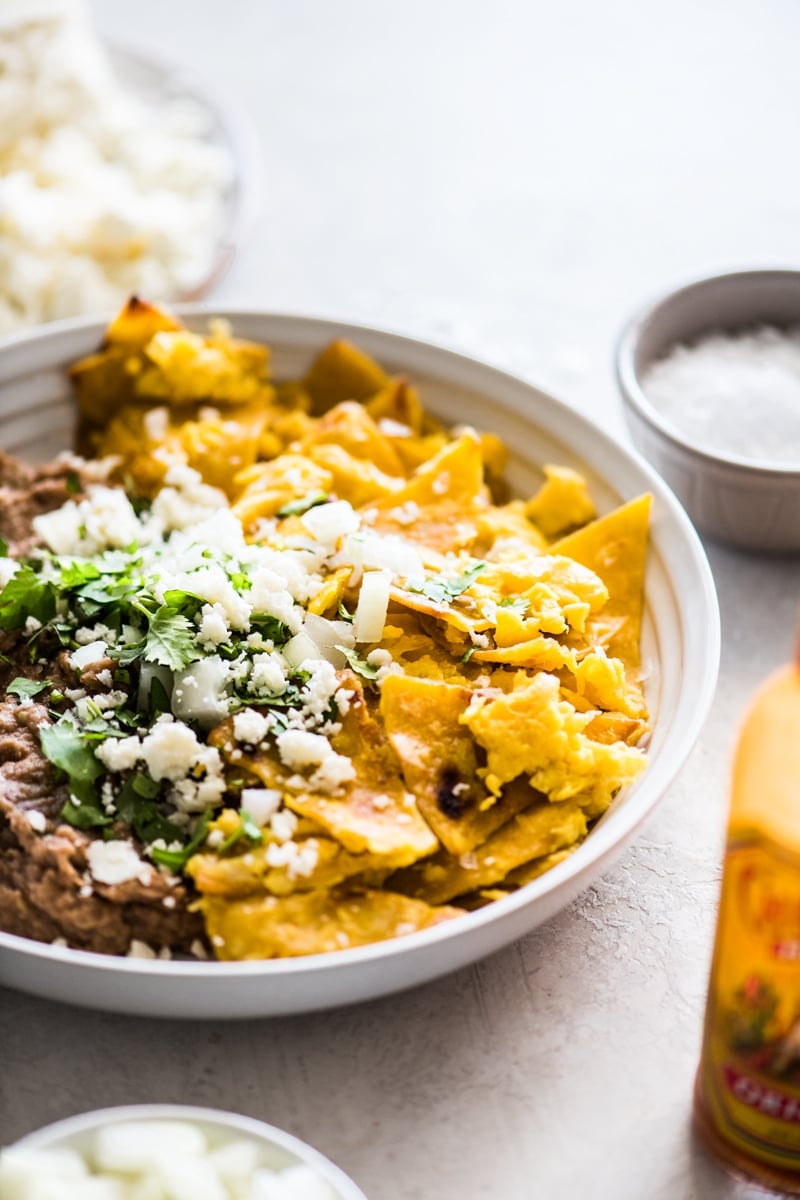 Migas recipe made from fried corn tortillas and eggs in a bowl with refried beans topped with queso fresco.