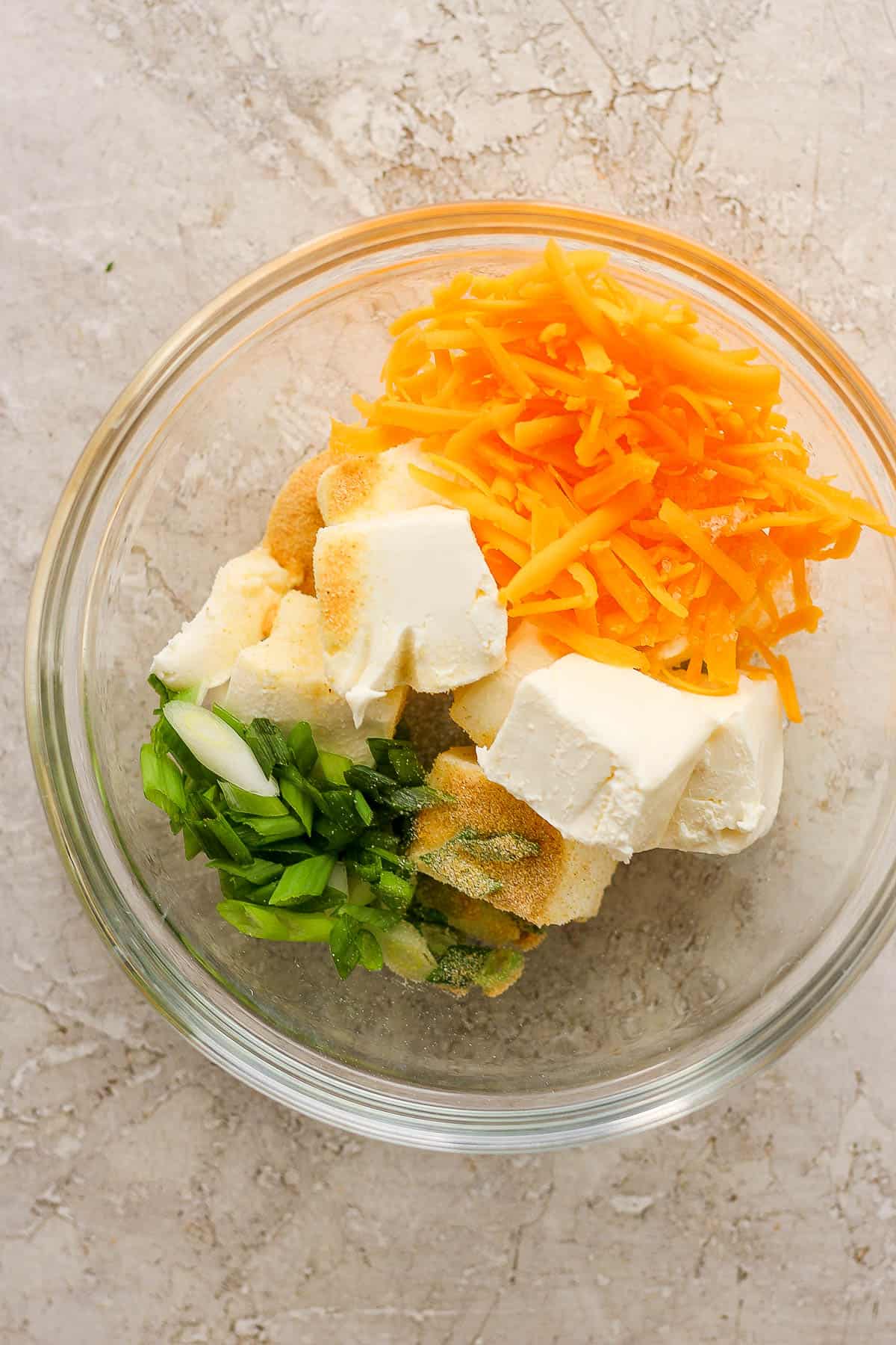 Cream cheese, seasonings, cheese, and green onions in a mixing bowl.